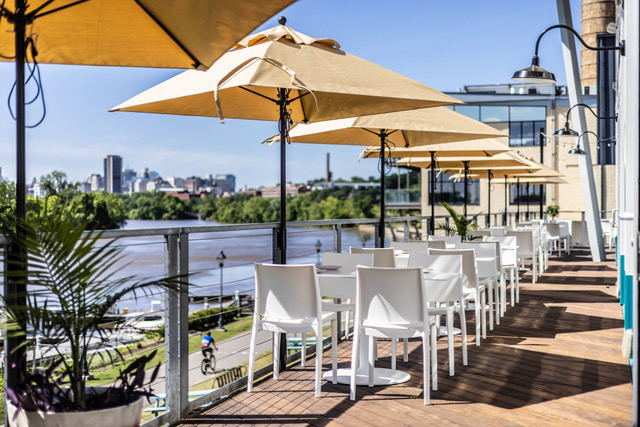 Riverfront Patio Dining at Rocketts Landing in Richmond, VA. Tables and beige umbrellas line the outdoor dining area at Island Shrimp Co. This Richmond seafood restaurant overlooks the James River and the Capital Trail. 